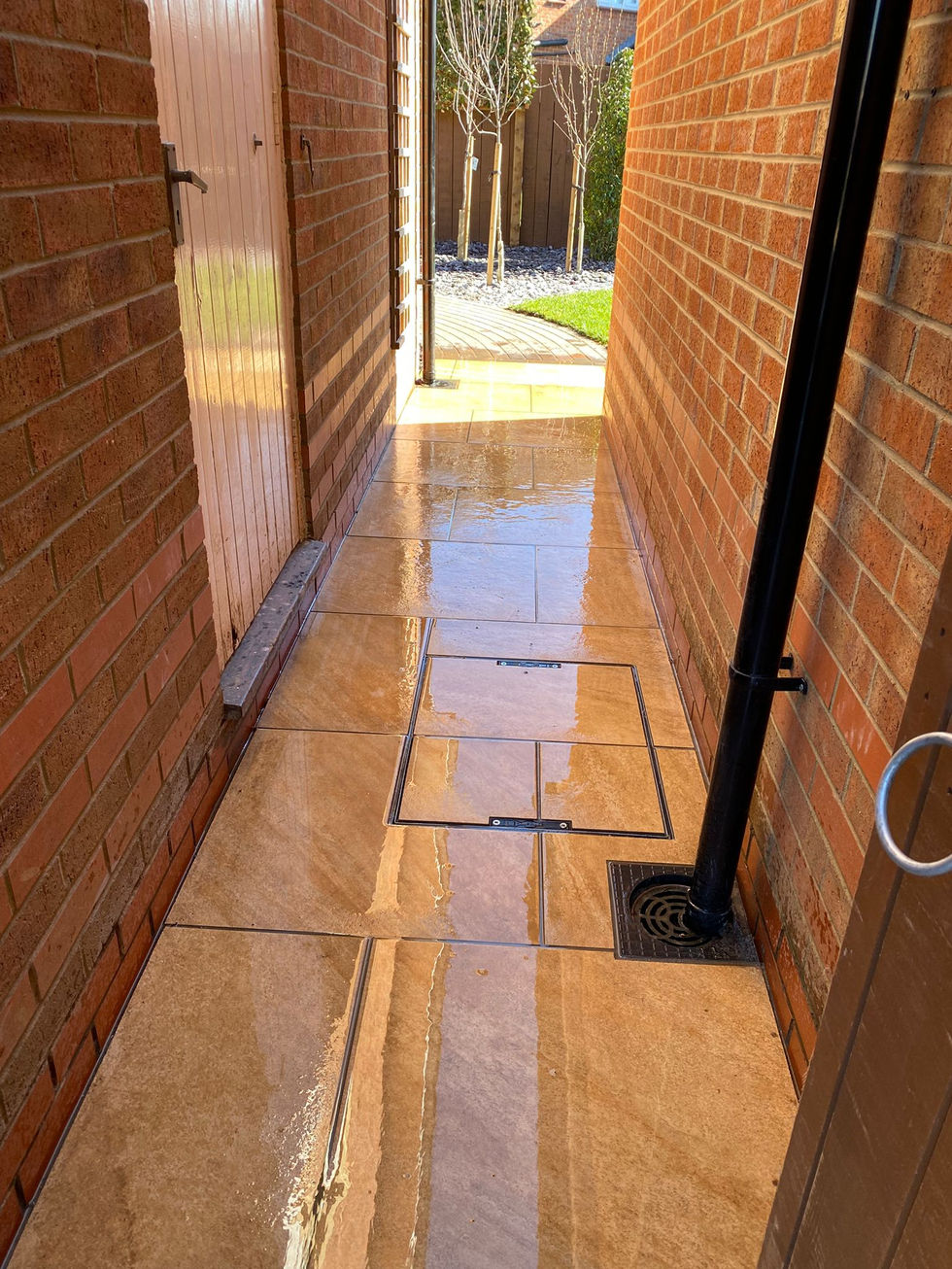 Project Overview:
This project focused on transforming a standard new-build garden into a clean, functional outdoor space designed for modern family living. The brief was to create a low-maintenance garden with strong visual structure, usable zones, and year-round interest.
⸻
The Design:
The layout was carefully considered to balance open lawn space with defined planting and entertaining areas. A central lawn provides a practical space for family use, while curved pathways and circular patio features introduce movement and soften the overall design.
Porcelain paving was selected to deliver a contemporary finish with durability and minimal upkeep. The warm tones complement the surrounding brickwork and help unify the space.
Raised beds and retained borders were introduced to manage levels and create depth, using natural stone to contrast against the clean paving lines. These features also provide structured planting zones that will mature over time, adding colour and texture to the garden.
⸻
Key Features:
• Porcelain patio and pathways for a modern, low-maintenance finish
• Circular feature patio creating a focal point within the garden
• Central lawn area for practical family use
• Raised stone retaining walls adding structure and interest
• Decorative gravel beds for drainage and low upkeep
• Structured planting scheme designed for year-round appeal
• Defined side access with integrated drainage solutions
⸻
The Result:
The finished garden is a well-balanced outdoor space that combines clean, contemporary design with practical functionality. The layout offers clear zones for relaxing, entertaining, and everyday use, while the planting will continue to soften and enhance the space as it establishes.
A great example of how thoughtful design and quality materials can transform a garden into a space that not only looks good on day one, but continues to improve over time.