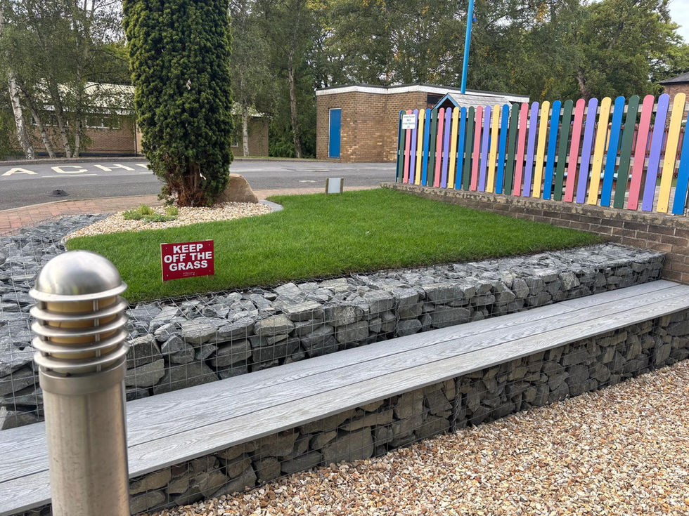 Raised lawn area at Teesside High School with gabion stone wall and timber seating, constructed by Wilkinsons Landscapes.