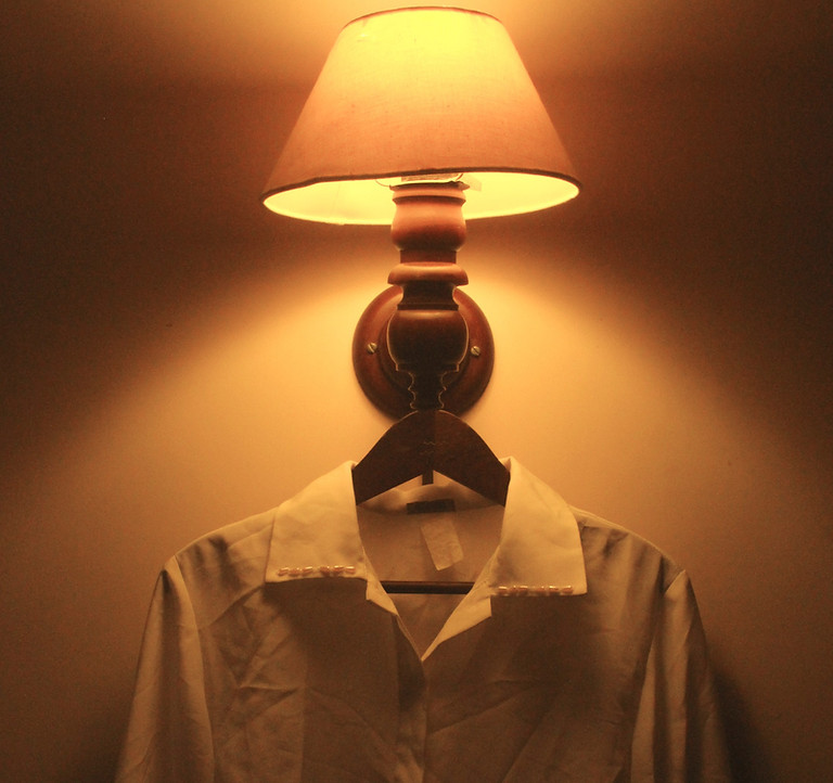 foto com luz alaranjada de um abajur e roupa pendurada