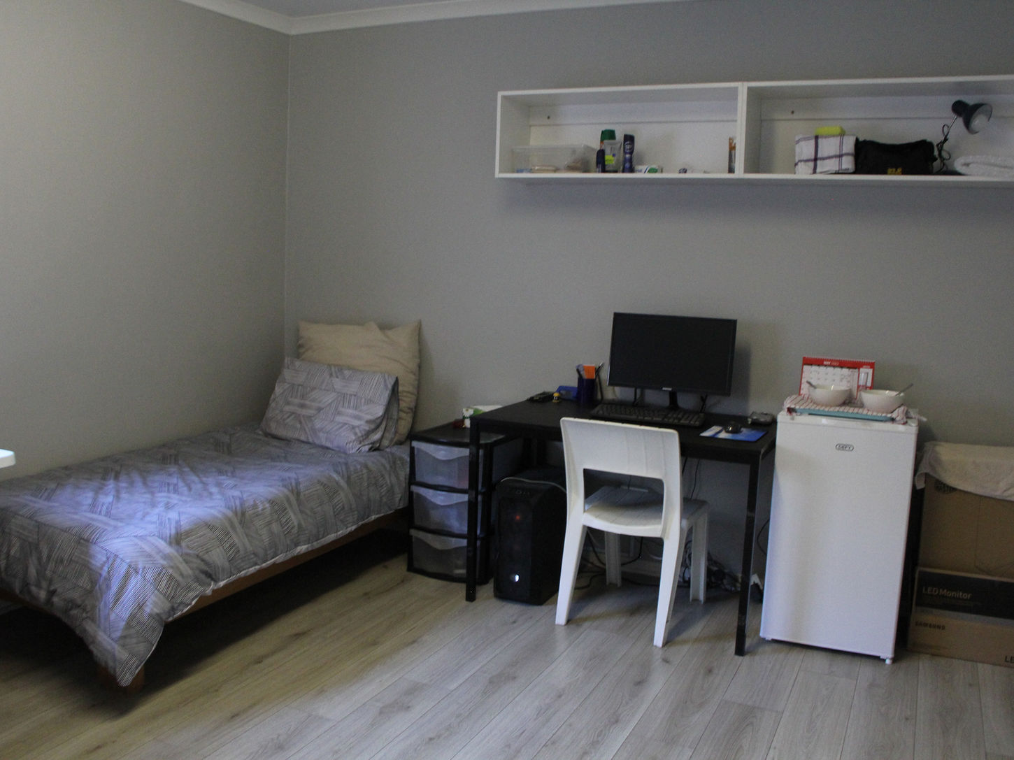 Bedroom for one student that includes a desk, storage, and mini fridge.