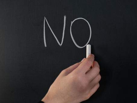 Hand writing "NO" in white chalk on a blackboard.