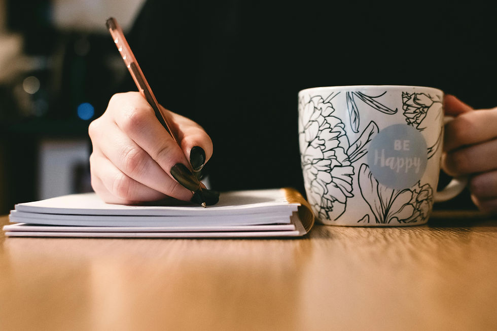 Handwriting in a notebook, holding a floral mug labeled "Be Happy." Relaxed setting with soft lighting, conveying a calm mood.