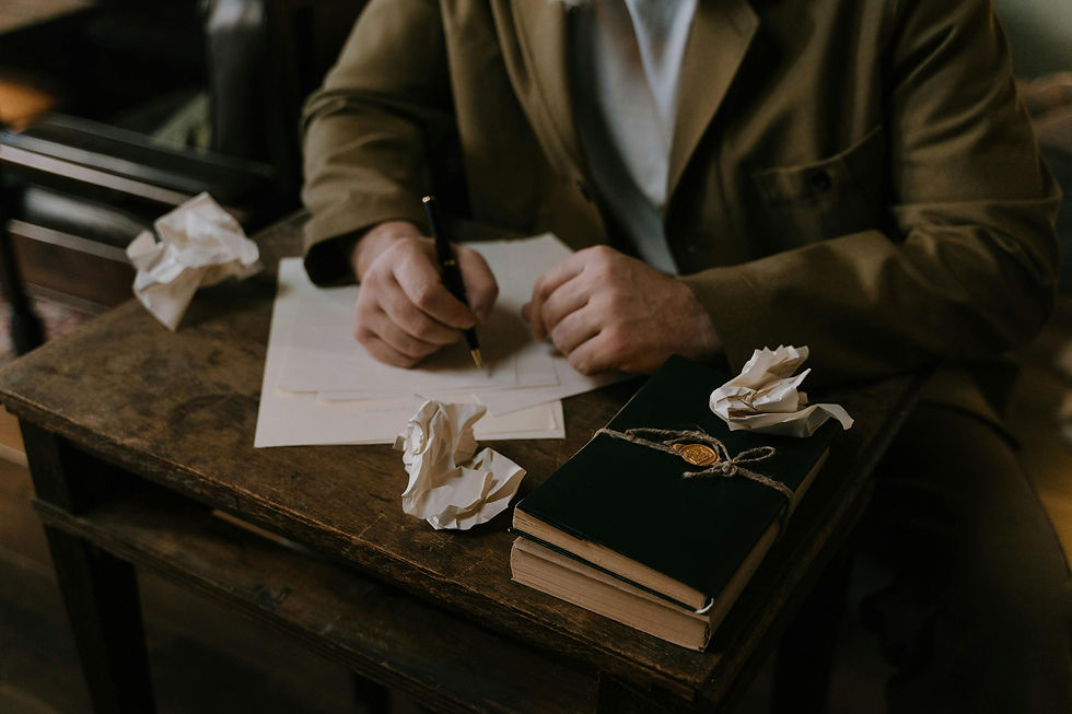 A person writing at a wooden desk surrounded by crumpled papers, a green wax-sealed notebook. Mood is thoughtful and focused.
