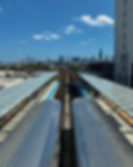 View of two silver trains at a station, with a city skyline in the background under a clear blue sky. Minimalist urban scene.