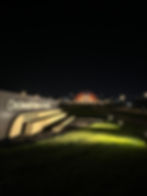 Night view of Cincinnati Union Terminal sign and illuminated building in distance. Green grass with spotlights. Calm, serene ambiance.