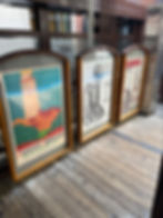Framed vintage posters on a wooden floor: Evanston Lighthouse, Automatic Telephone, and Bearings. Background features city architecture.