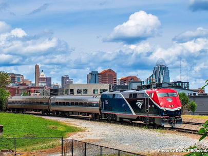 Amtrak's Cardinal passing through a Kentucky railroad track with the Cincinnati skyline behind it.