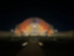 Art Deco Cincinnati Union Terminal with arched facade illuminated in orange at night. Pathway and lights lead to the entrance. Dark sky background, symmetrical design.