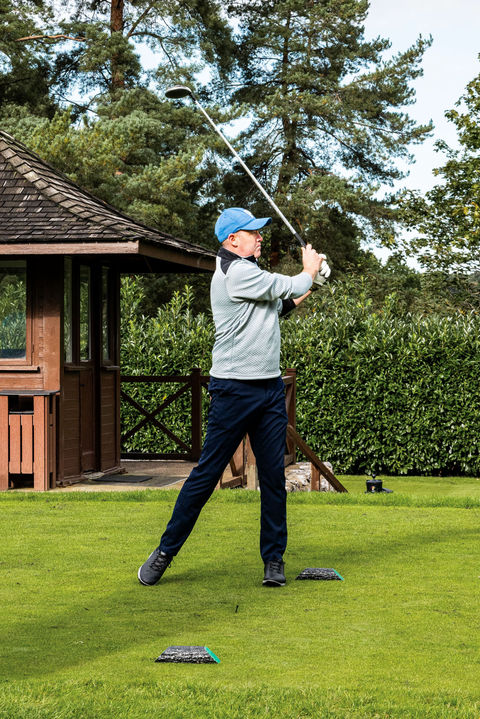 event photography of a man in a blue hat swinging a golf club