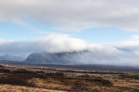a mountain covered in clouds with a blue sky in the background