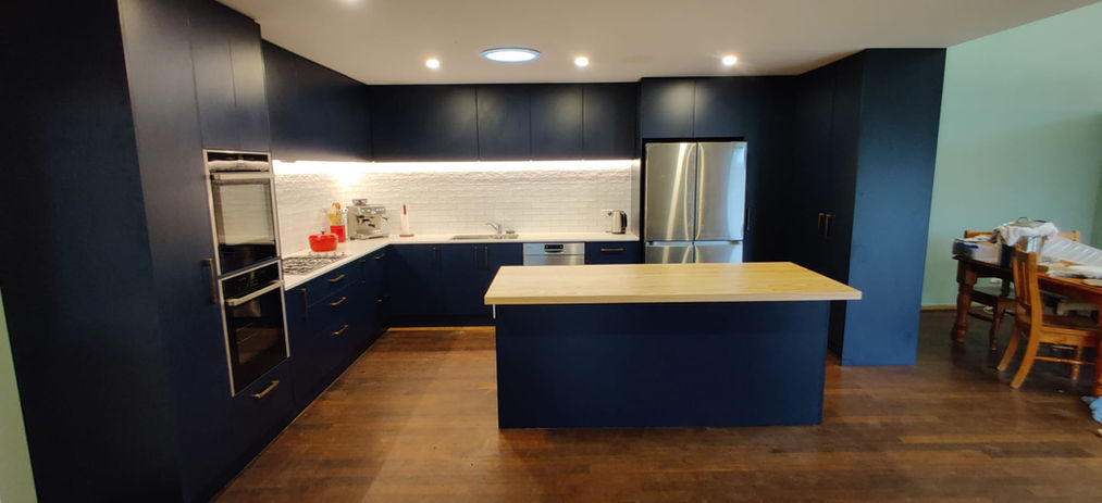 An open plan kitchen featuring a central island, under cabinet LED lighting, dark blue cabinetry and integrated appliances.
