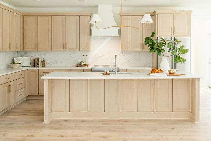 large kitchen with warm wood cabinets, brass lighting, brass hardware, chrome faucet, and decor on countertops. full height stone backsplash. 