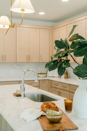 close up of large kitchen with warm wood cabinets, brass lighting, brass hardware, chrome faucet, and decor on countertops. full height stone backsplash.