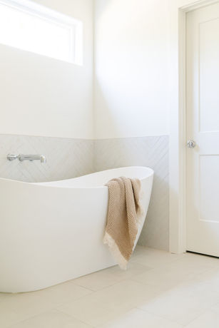 white tub with tile on wall behind. chrome delta tub filler. towel elegantly draped over edge