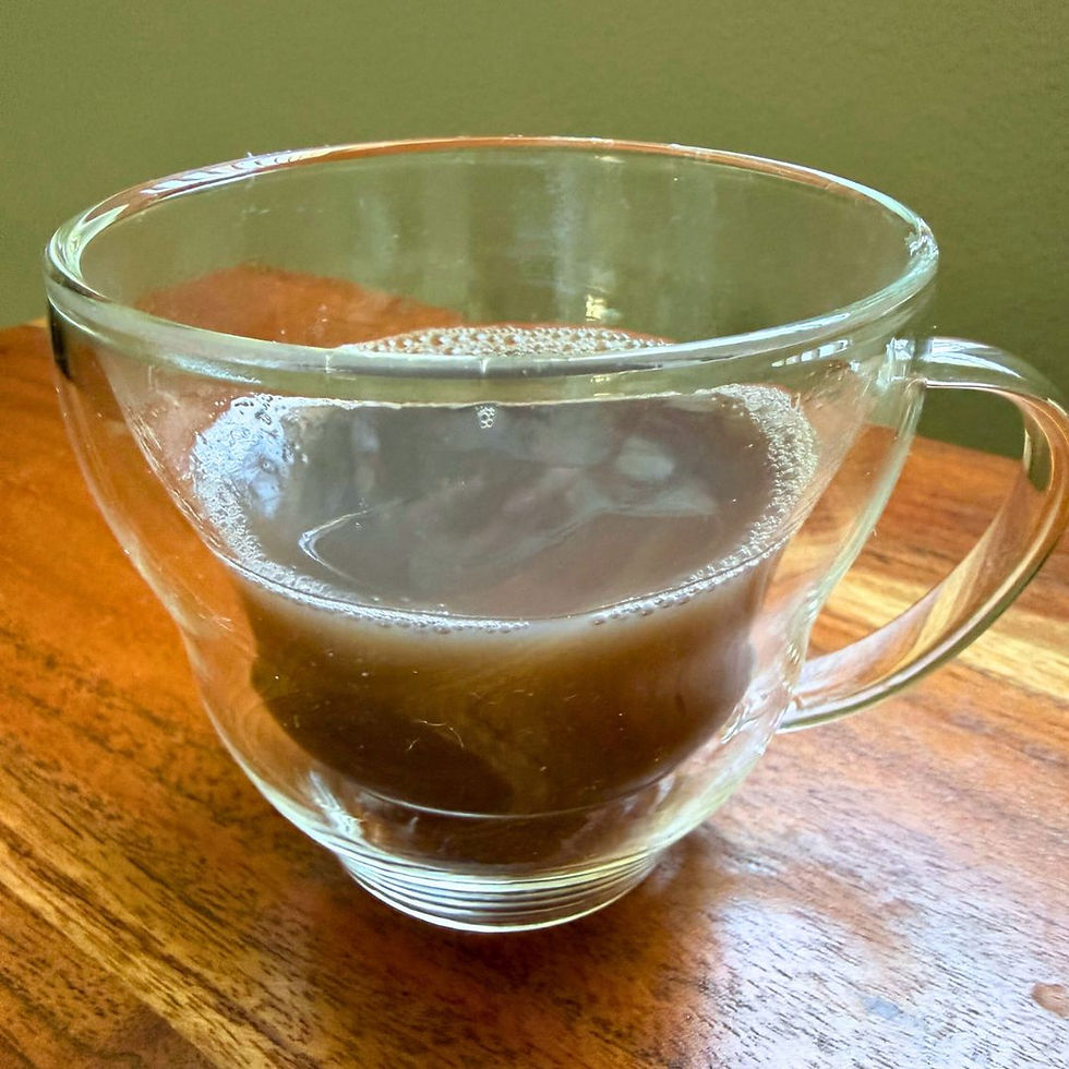 Clear glass mug with azuki cooking liquid on a wooden table. The background is plain and light, giving a cozy, warm atmosphere.