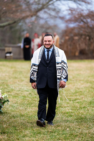 A smiling wedding officiant walking down the aisle, wearing a prayer shawl.