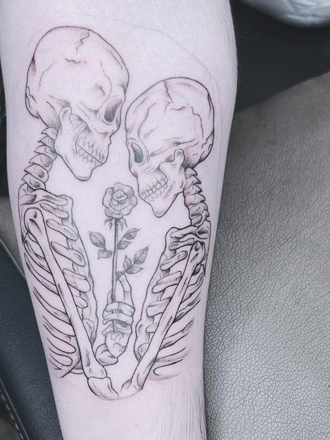 Romantisches, feines Linework-Tattoo zweier Skelette auf dem Arm, die sich gegenüberstehen und gemeinsam eine Rose halten, gestochen im Tattoo-Studio Neuanstich.