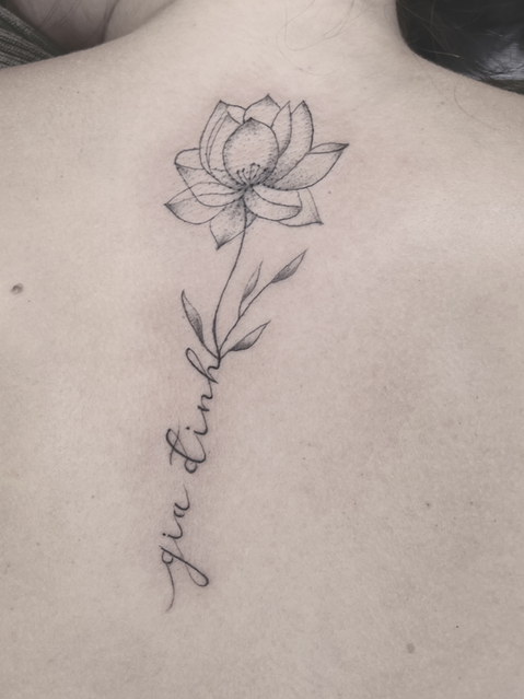 Zartes Fineline-Tattoo auf dem Rücken mit einer eleganten Lotusblüte, deren Stiel fließend in einen geschwungenen Schriftzug übergeht, umgesetzt bei Neuanstich in Horneburg Landkreis Stade.