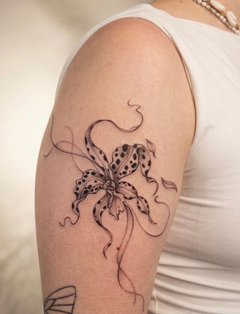 Fineline-Tattoo einer Orchidee mit gepunktetem Muster auf den Blütenblättern und elegant geschwungenen, fließenden Linien auf dem Oberarm, gestochen bei Neuanstich in Horneburg.