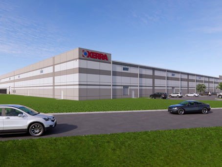 A digital rendering of OXERRA’s new 120,000-square-foot warehouse in Augusta, Georgia, shows a modern gray-and-white industrial building with the OXERRA logo, surrounded by parked cars and green lawn under a clear blue sky.