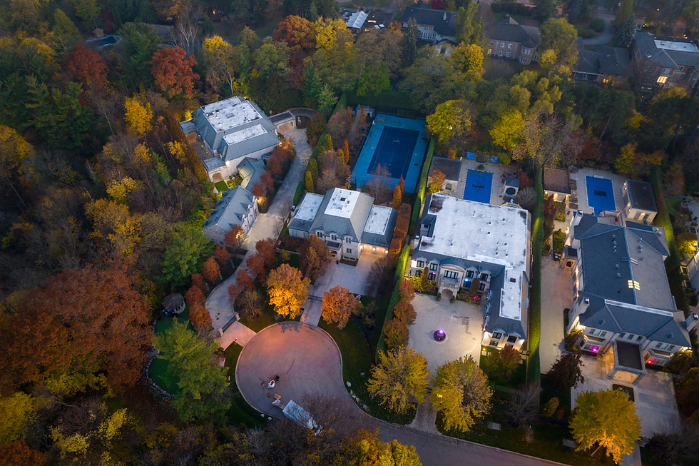 Aerial view of luxurious homes surrounded by colorful autumn trees, with brightly lit driveways and a central blue tennis court. Tranquil mood.