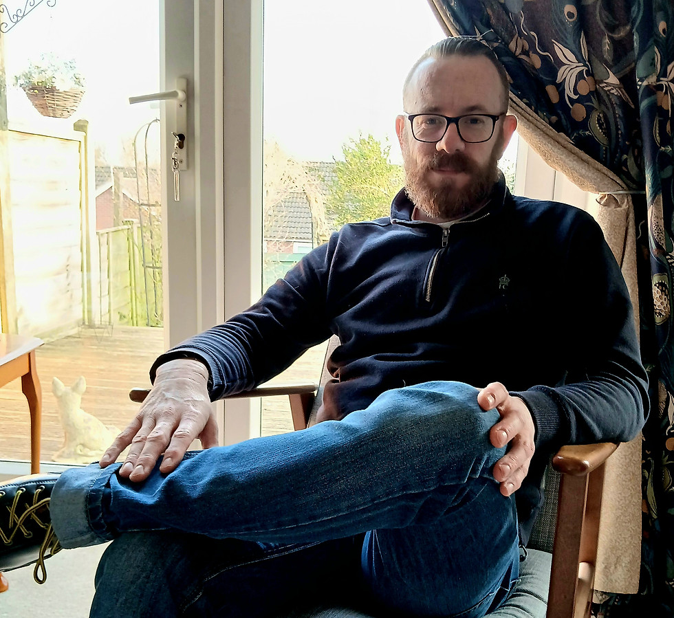 Image of Stu sitting in a chair, ready to listen to you. He wears glasses and has a beard.