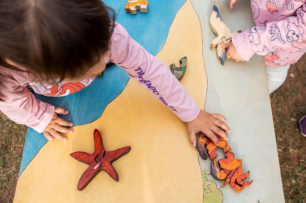 Una chica poniendo una pieza de puzzle de cangrejo en una mesa de juego de madera con una estrella de mar, pájaros y otros animales marinos.
