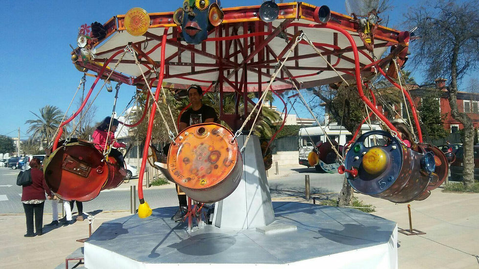 Un carrusel fet amb bidons i cadires, gent gaudint a l'aire lliure.