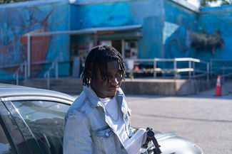 Man in a denim jacket standing by a car near a blue mural