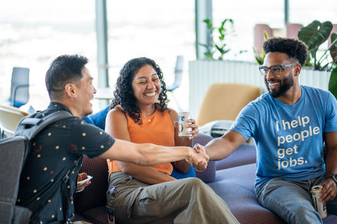 Three diverse people smiling and shaking hands, text on shirt reads 'I help people get jobs.'