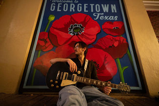 Man with electric guitar before Georgetown Texas poppy mural