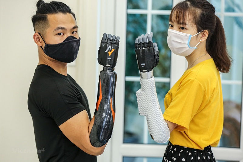 Hai người khuyết tật đang sử dụng tay điện chức năng của Vulcan và chụp hình cùng nhau