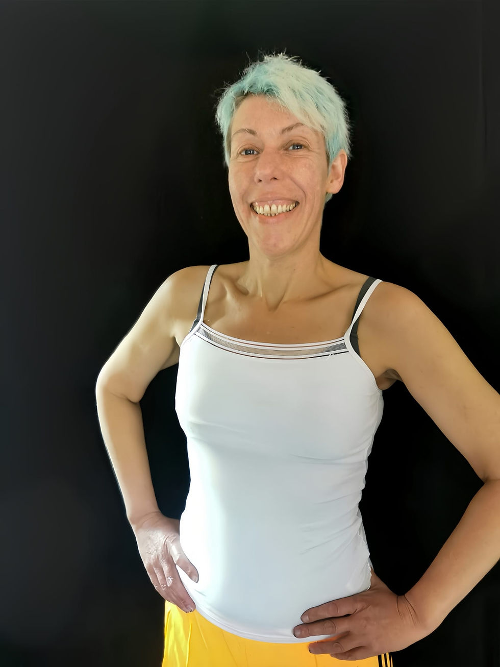 Women's health therapist standing confidently, hands on hips, smiling in a clinic setting.