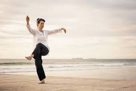 Woman practicing Tai Chi on the beach at sunrise, illustrating the Contemporary Tai Chi Class and the connection between wellness and coastal living.