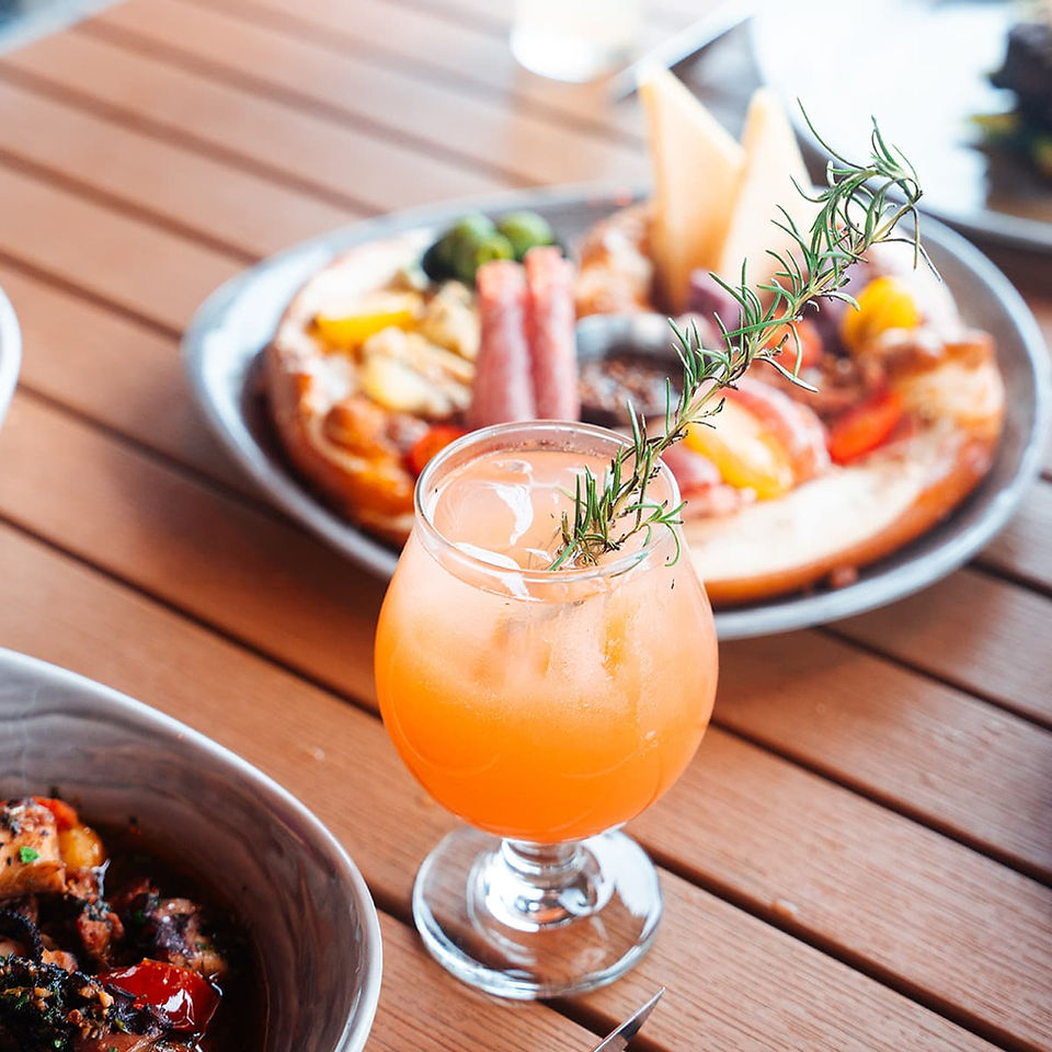 Signature orange craft cocktail garnished with fresh rosemary served alongside shareable coastal appetizers.
