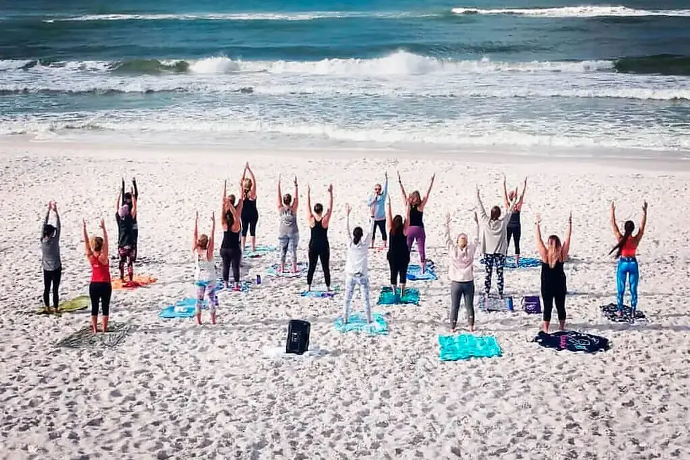 Group of participants practicing yoga together on a white-sand beach overlooking the Gulf of Mexico during a coastal wellness retreat.