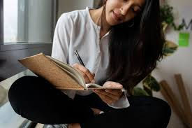 Woman seated indoors journaling in a notebook, representing the Coastal Journal Writing Group event focused on creativity, reflection, and community connection.
