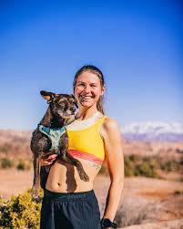 Cat Bradley stands atop a desert overlook in running gear with mountains in the distance, showcasing the confidence, focus, and resilience that have defined her ultramarathon career.