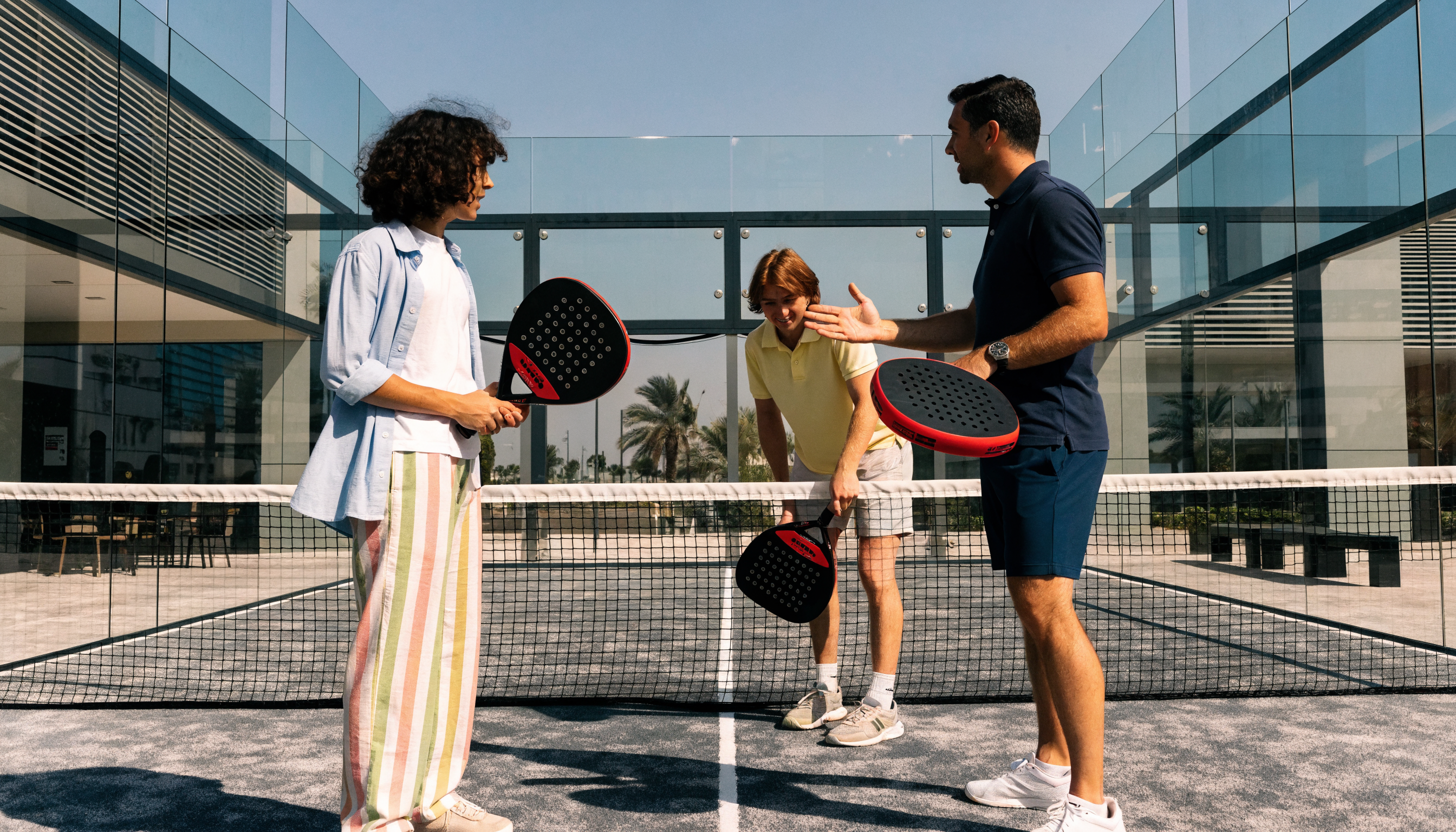 Two beginners taking their first padel lesson on an outdoor court in Dubai