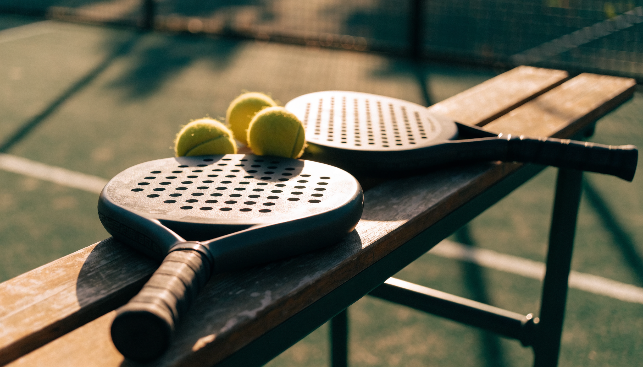Padel rackets and balls resting on a bench beside an outdoor court