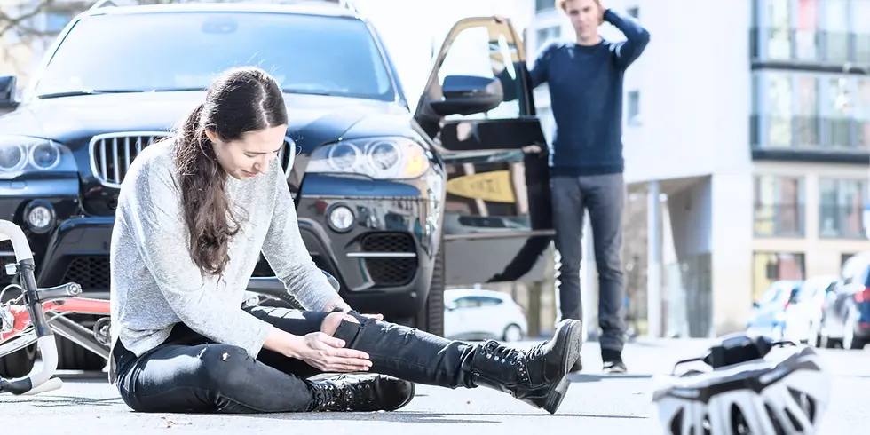 Woman sitting on the ground after a car accident holding her leg in pain.