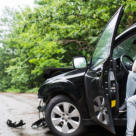 A person is sitting in the driver's seat of a car that has been involved in an accident