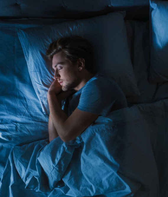 Person sleeping peacefully in bed under blue-toned lighting, representing restful sleep, an important factor for better blood sugar control.