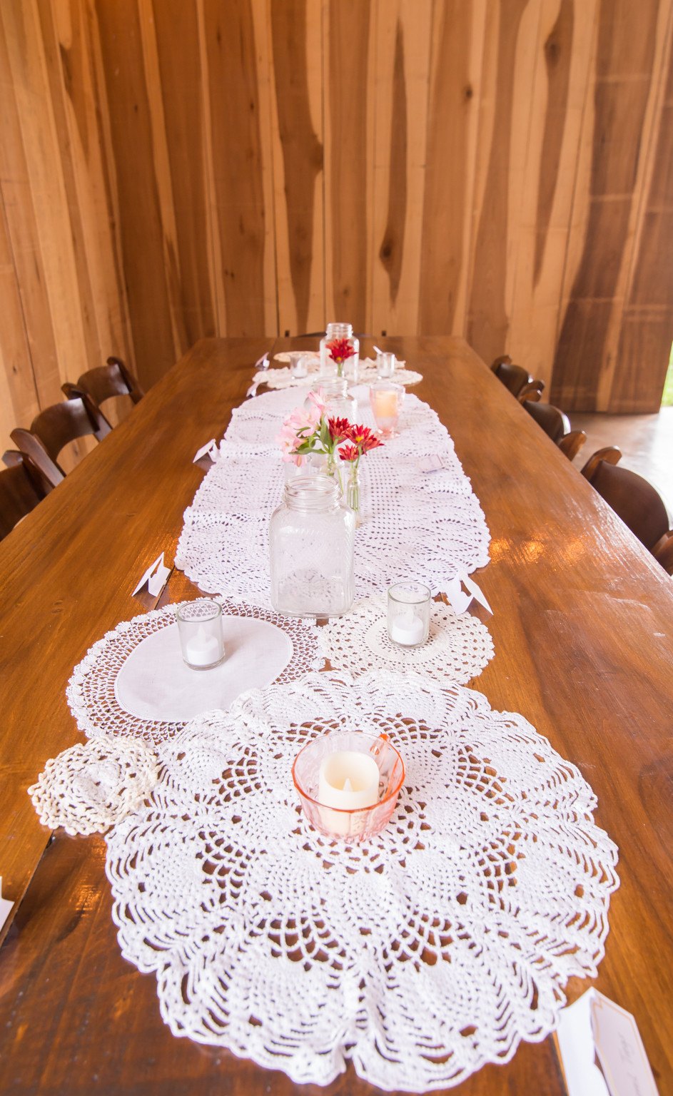Rustic wooden table set with lace doily runners, candles, and flower jars