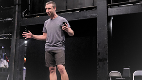Peter Fenton in a gray t-shirt standing on a black box stage leading a workshop
