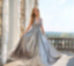 Frau in fließendem silbernem Abendkleid mit tiefem V-Ausschnitt, die das Kleid auf einer Terrasse mit Steinbalustrade