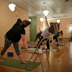 Yoga students practicing triangle pose using chairs