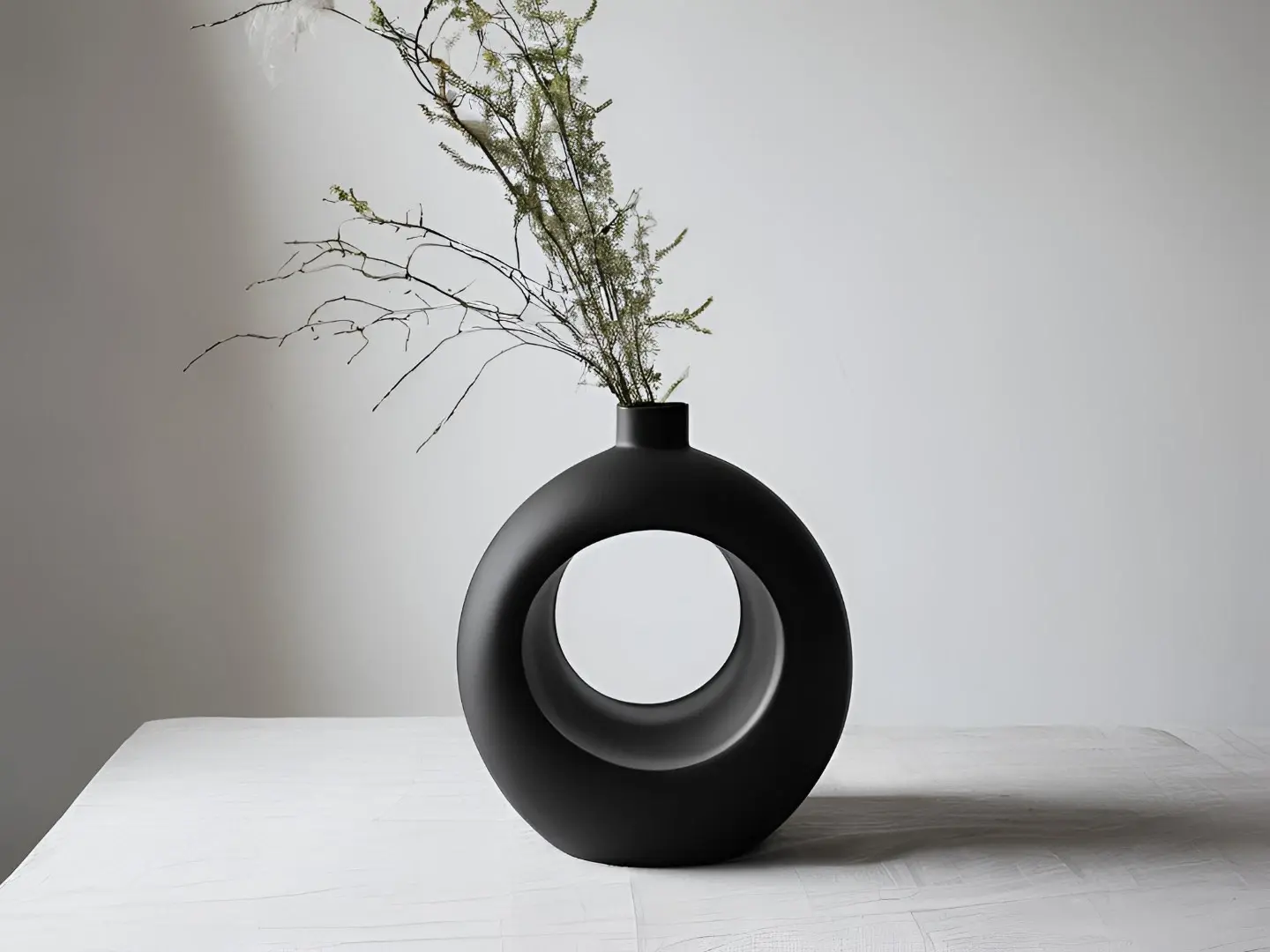 Vaso nero rotondo con foro centrale e foglie secche, minimalista.