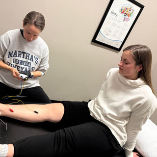 Practitioner applying functional dry needles to patient's leg during physical therapy session. 