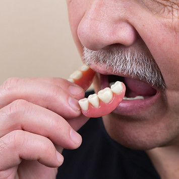 An old gray-haired man puts on his dentu